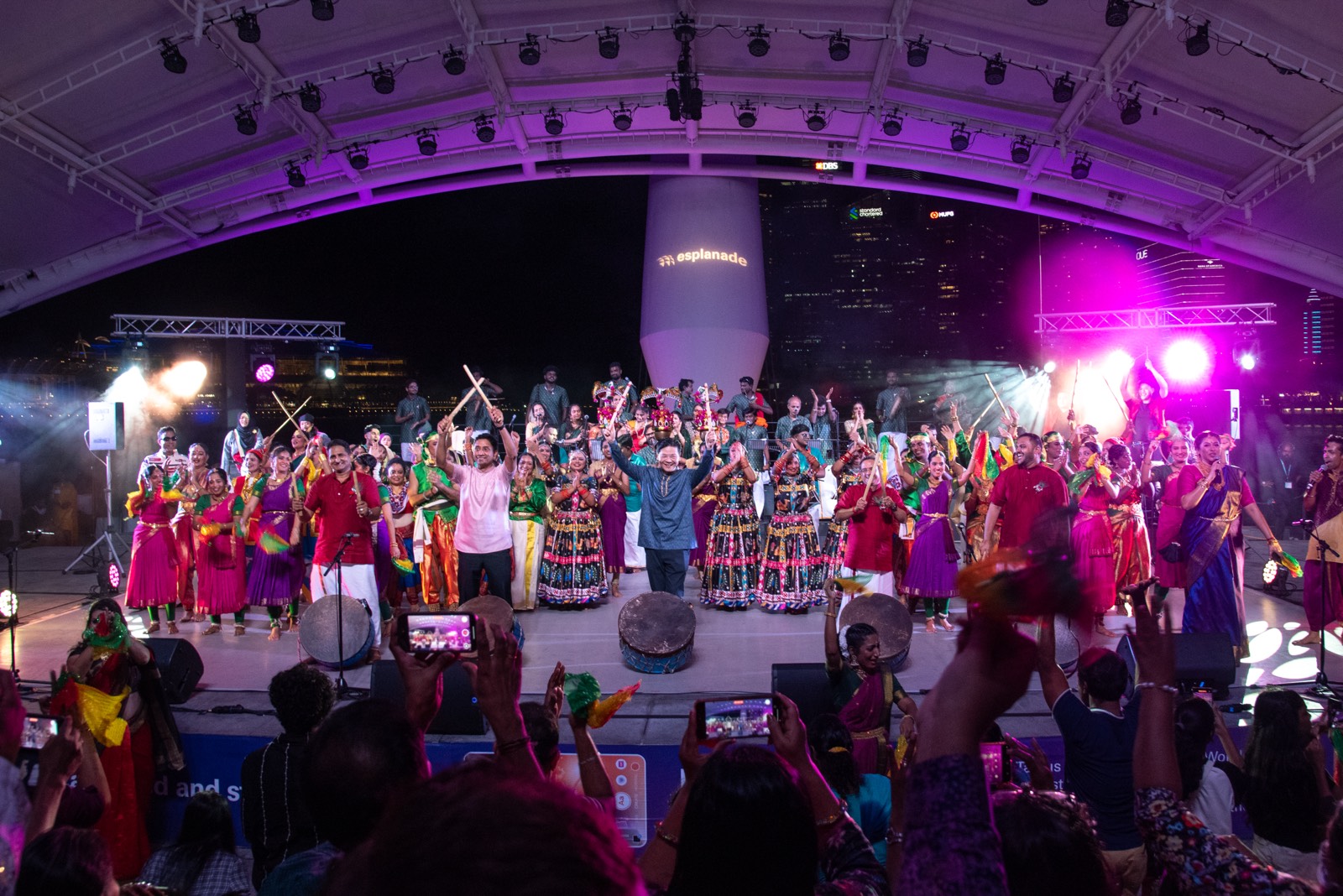 The full ensemble on stage at the Esplanade Outdoor Theatre, audience in the foreground